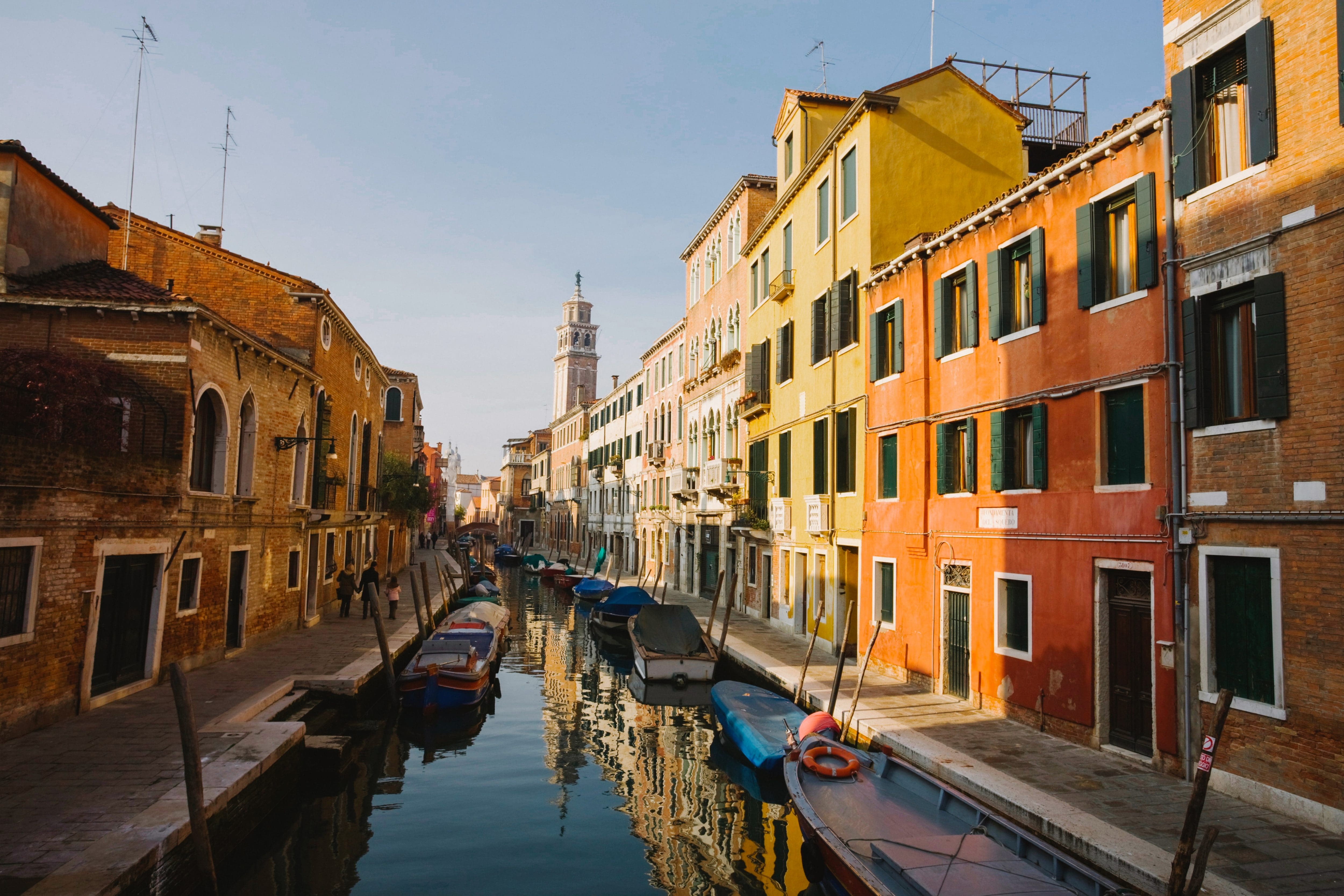 A quiet canal in Venice with parked gondolas and orange-hued houses at sun down