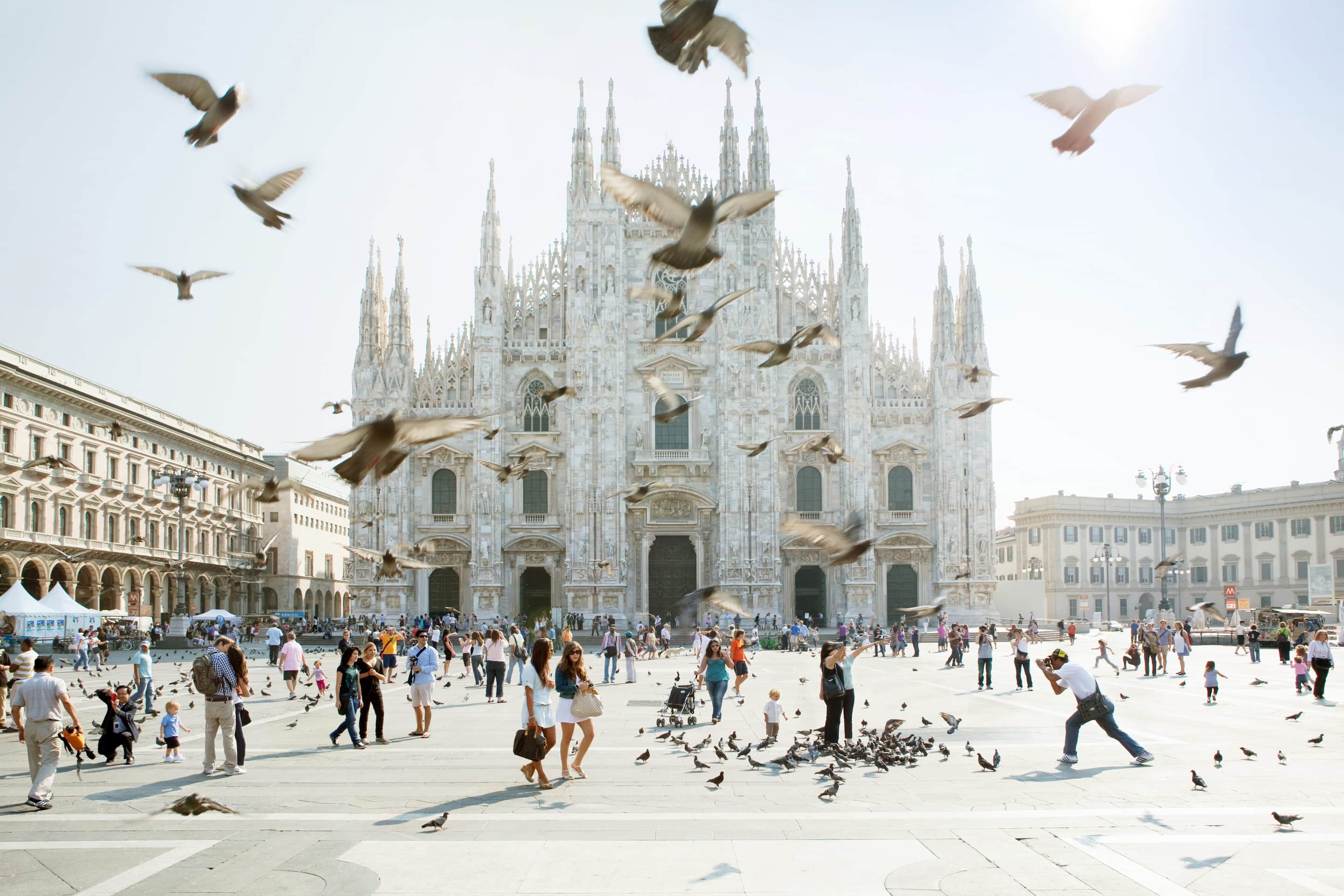 Birds flutter in the air in front of Milan's imposing white-facaded Duomo