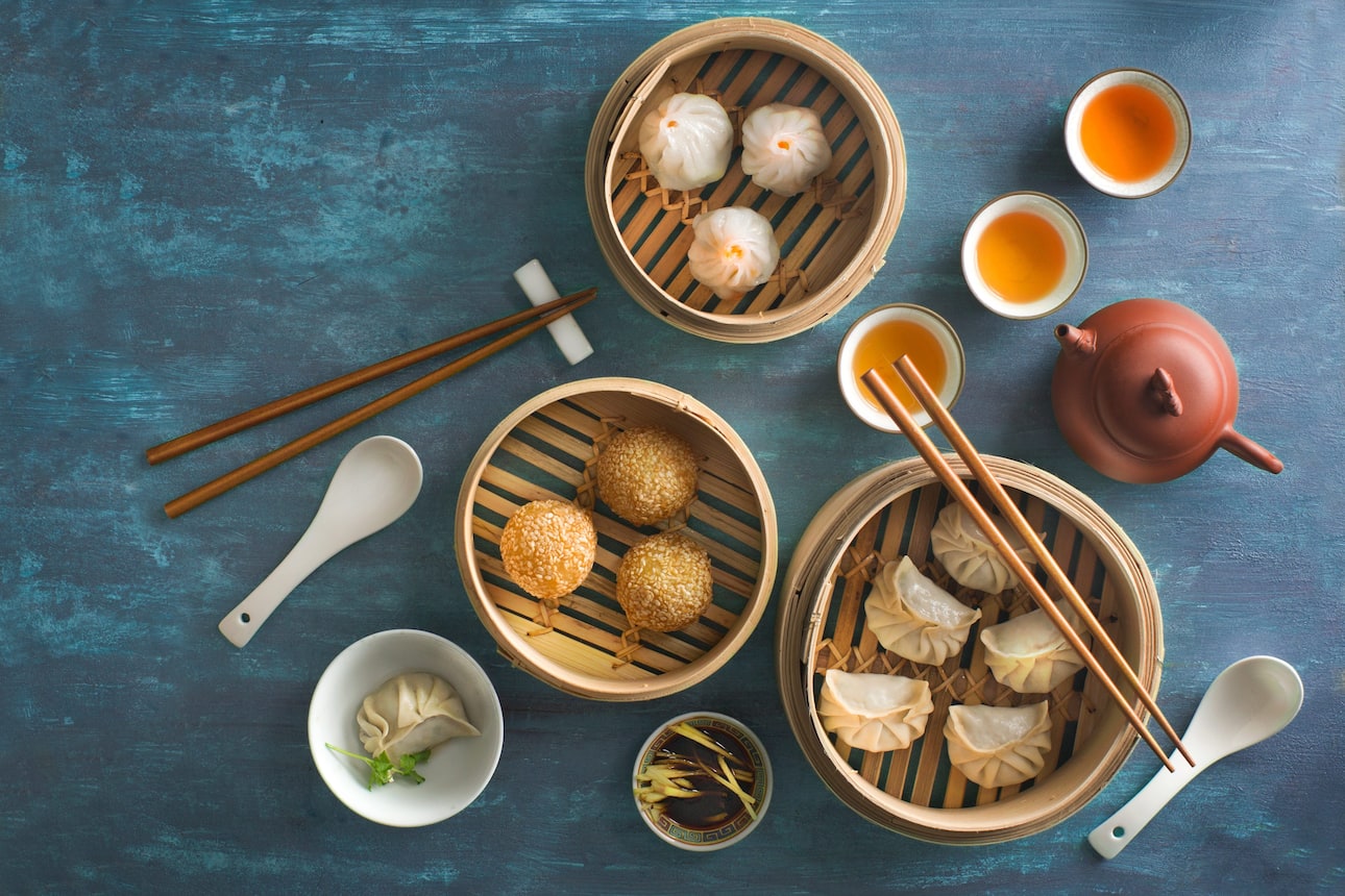 Selection of dim sum in bamboo baskets and two cups and pot of tea