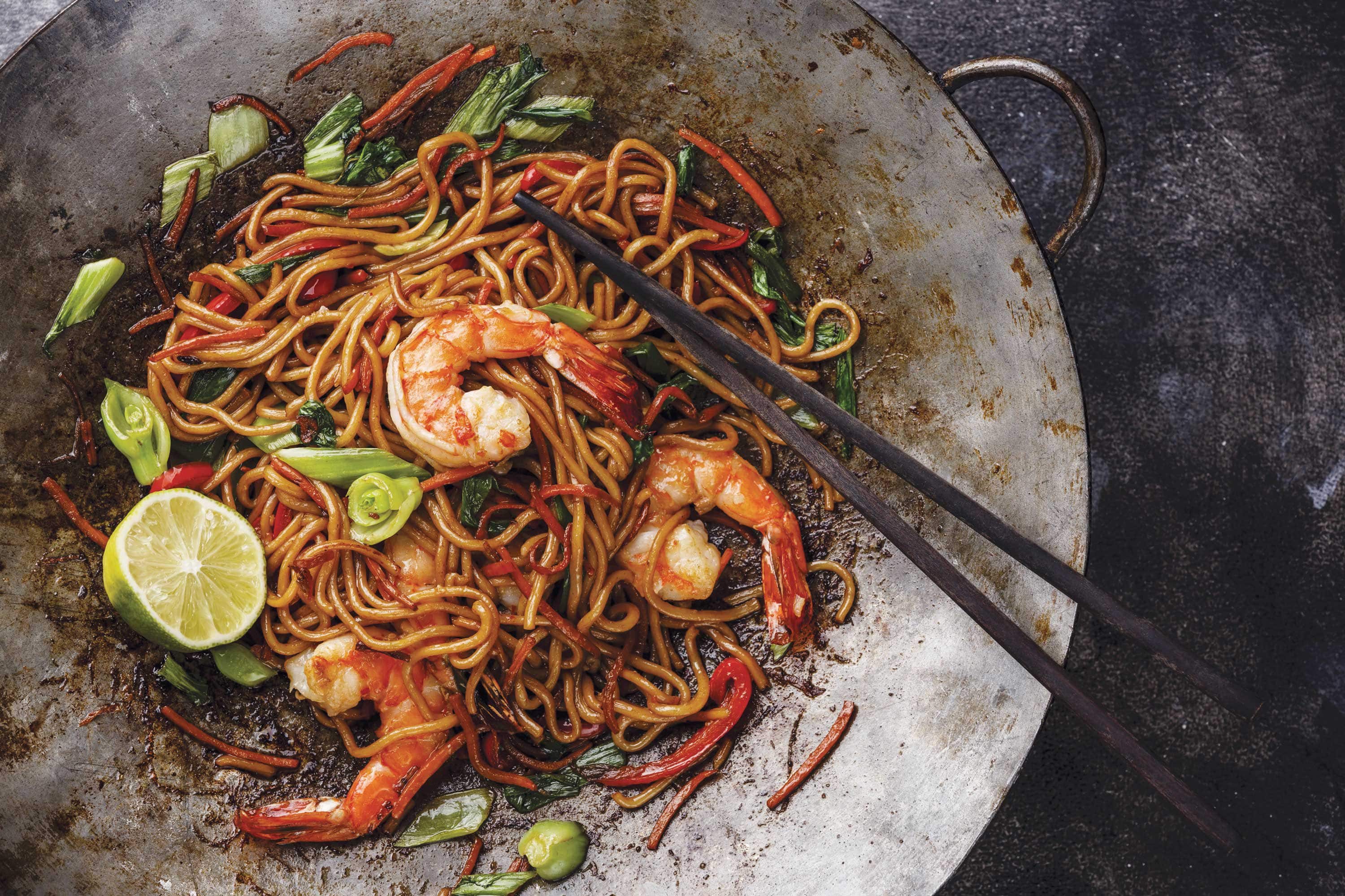 Fresh shrimp wonton noodles in a wok with chopsticks and half a lime