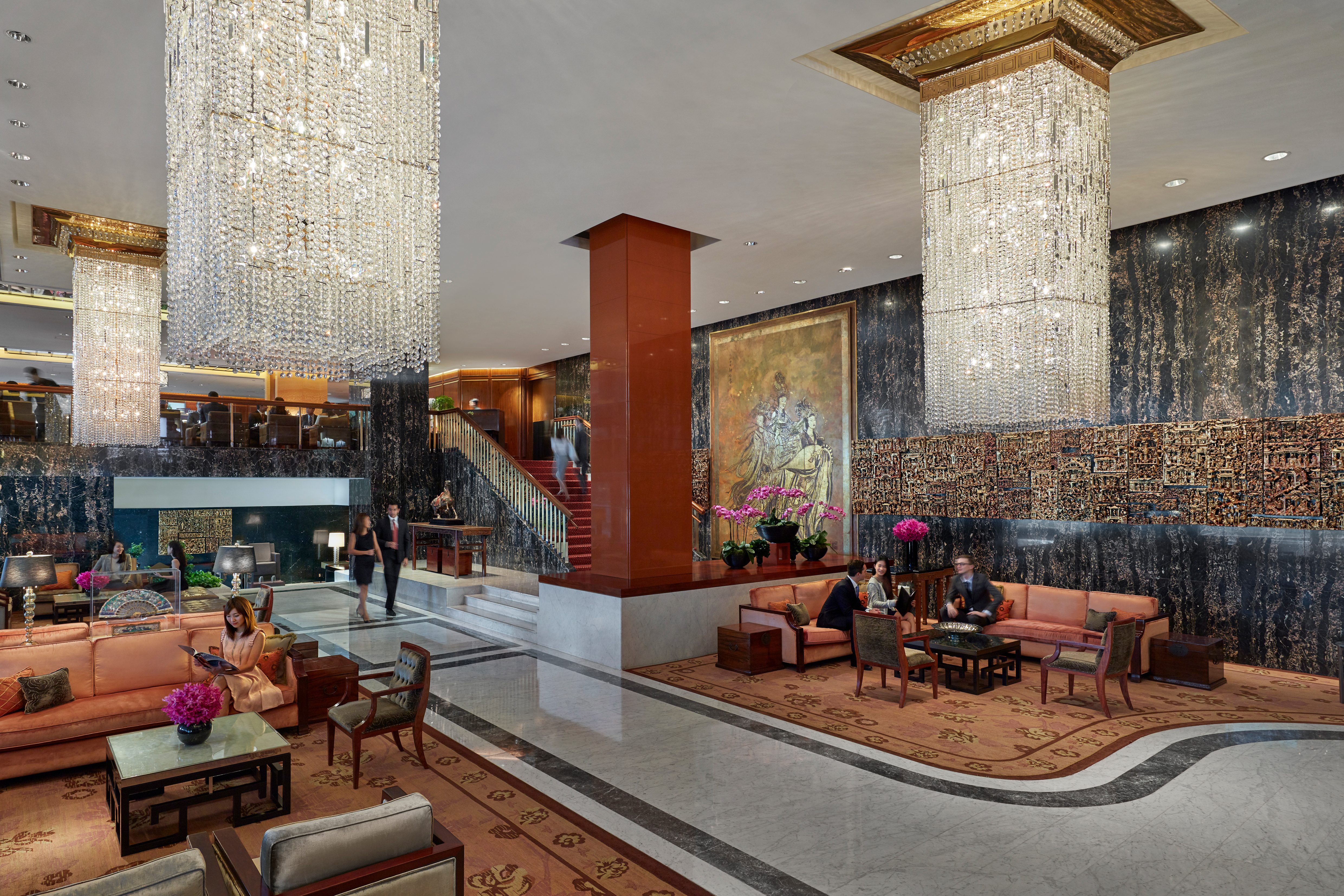 Elaborate crystal lighting fixtures hang above plush sofas where guests are seated inside Mandarin Oriental, Hong Kong