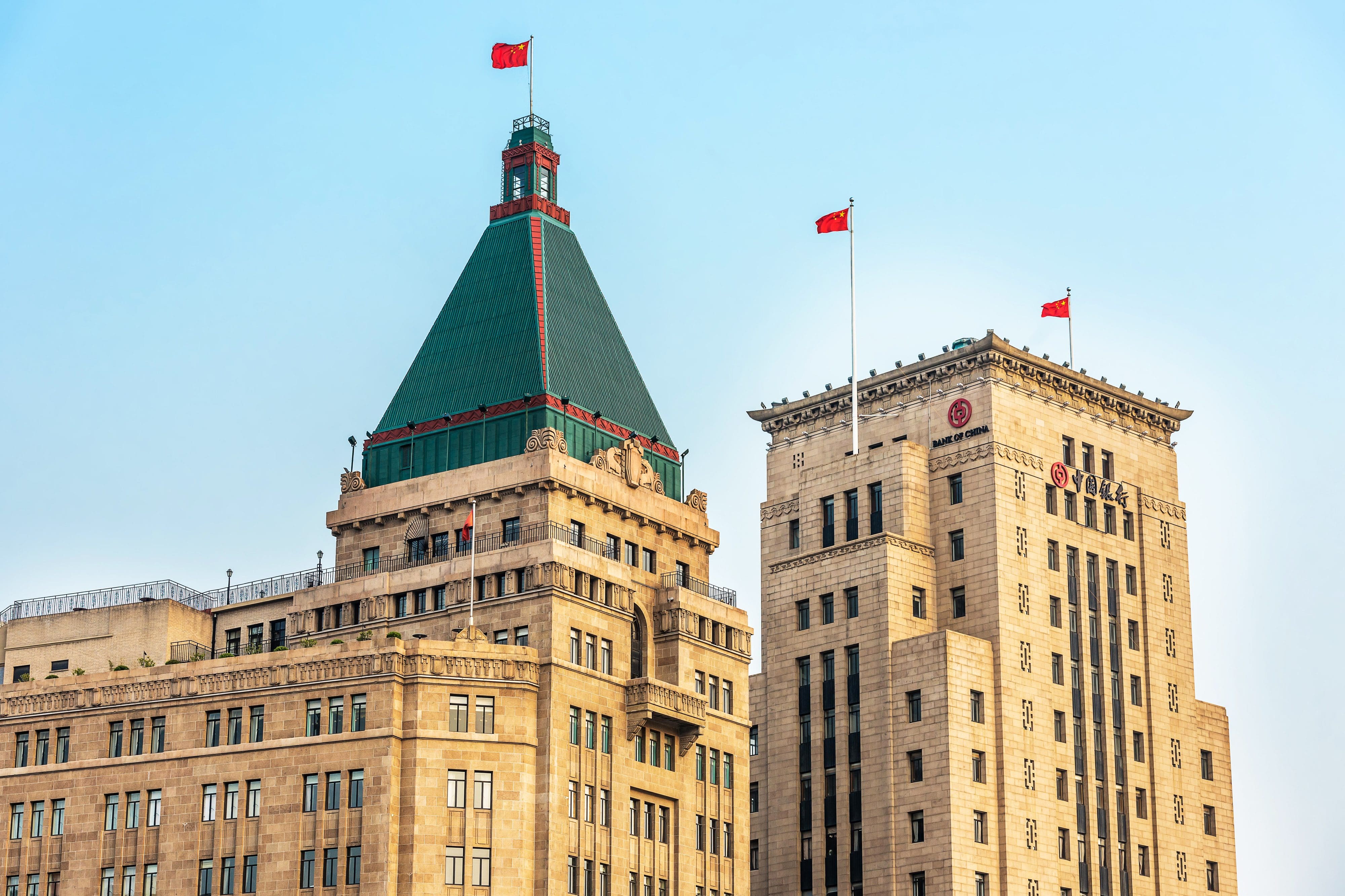 The top of the yellow stone Bank of China building with it green spire and red flags
