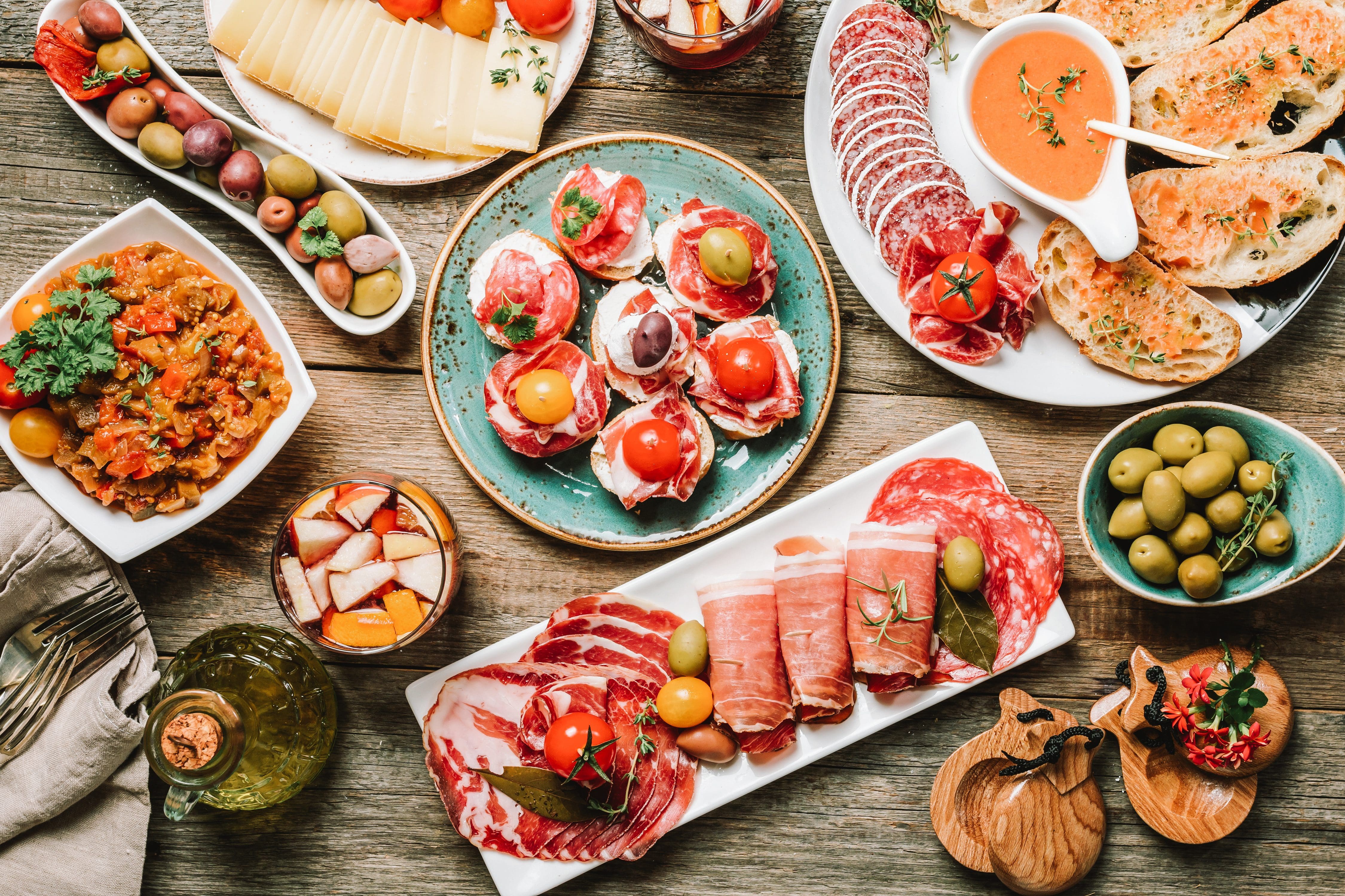 Overhead view of a table full of tapas dishes, from plump green olives to cured meats, cheeses, pan con tomate and olive oil