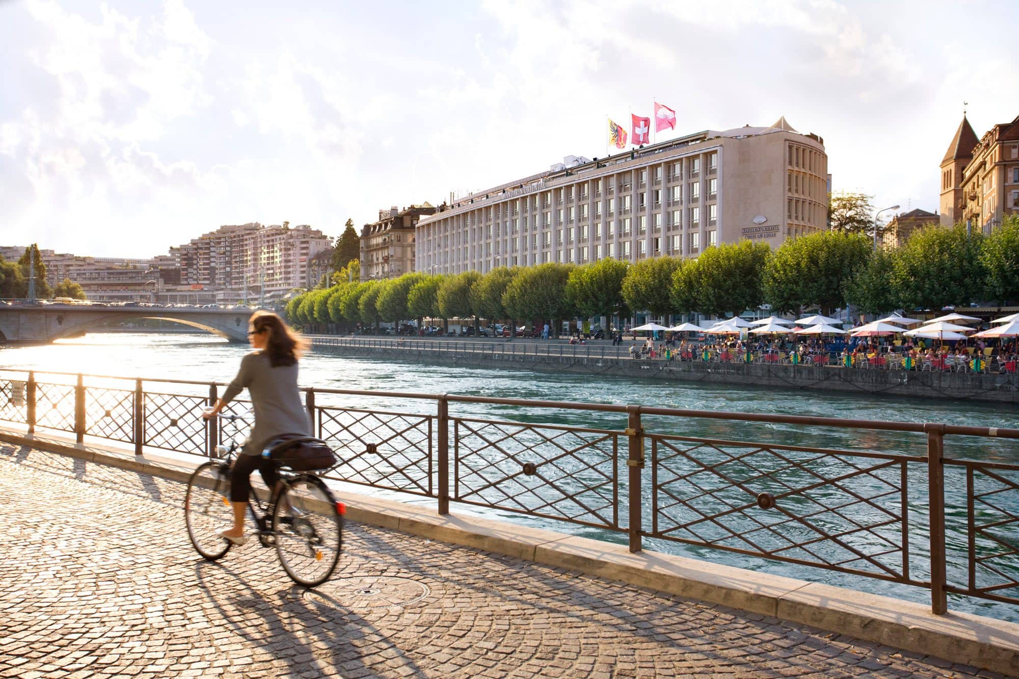 A woman rides a bike along the river across from Mandarin Oriental, Geneva