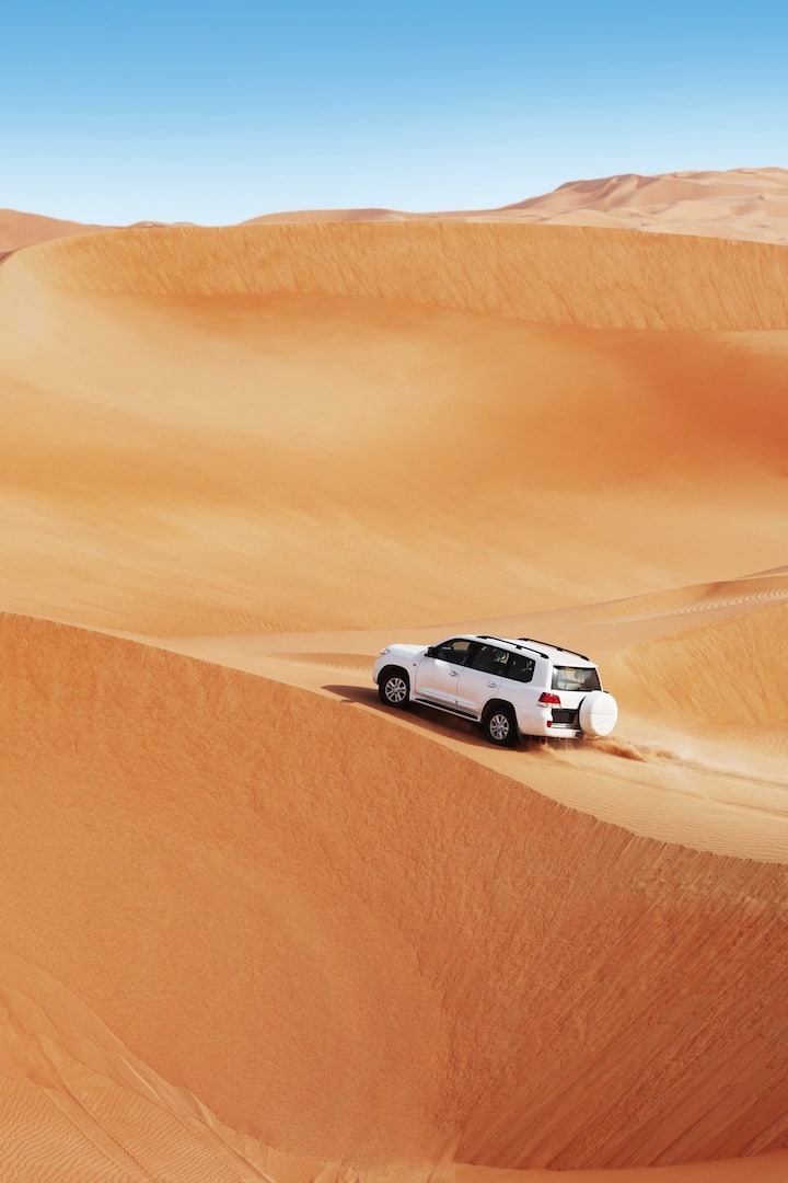 Four by four vehicle driving over desert dunes