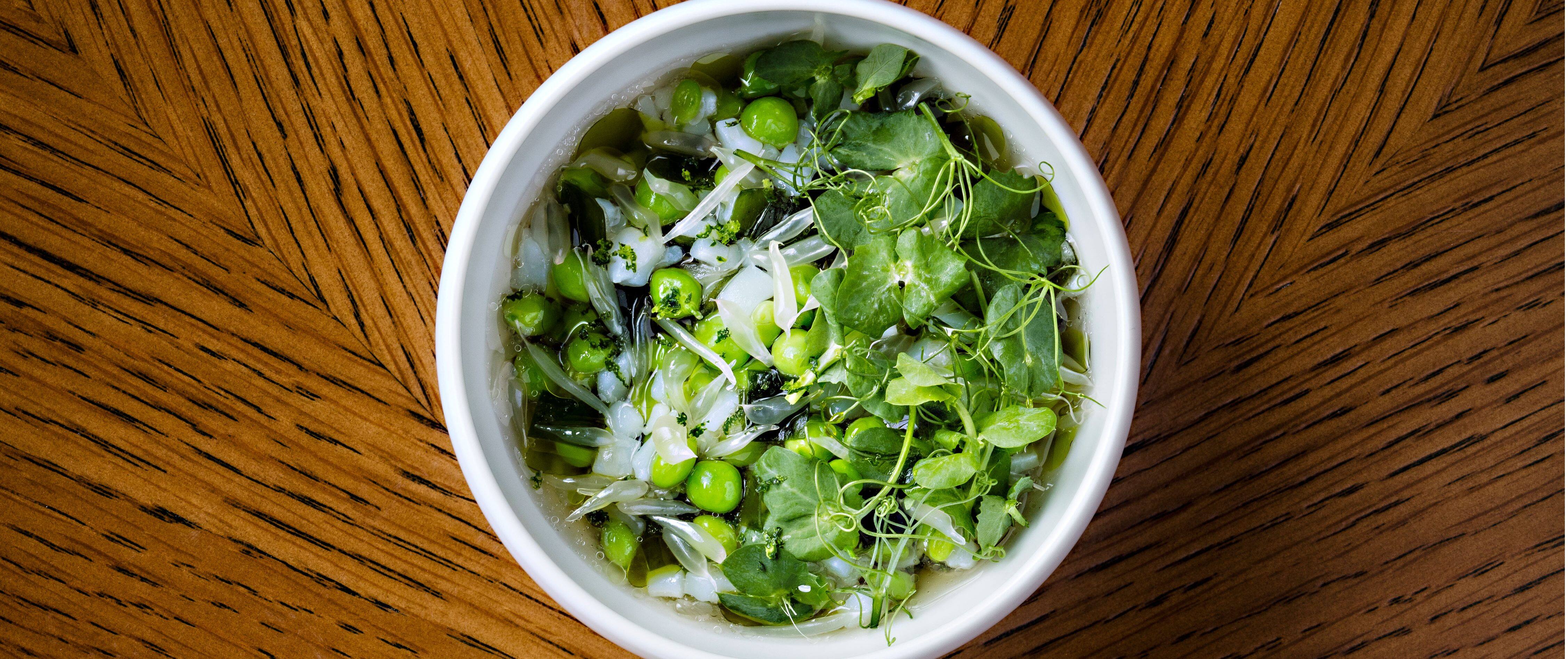 green peas in a white bowl on top of a brown wood table
