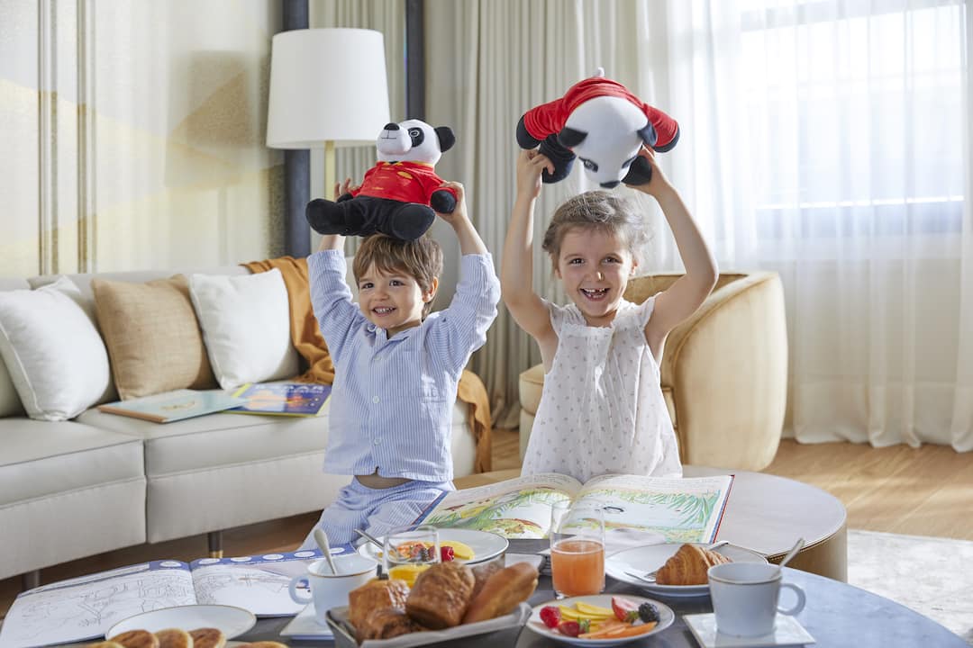 two kids playing on a bed with stuffed panda dolls